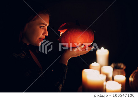 Young woman smiling with Halloween pumpkin Jack-o-lantern head in hand with candles. Female hands cutting pumpkins with knife Young woman smiling with Halloween pumpkin Jack-o-lantern head in hand with candles. Female hands cutting pumpkins with knife 106547100