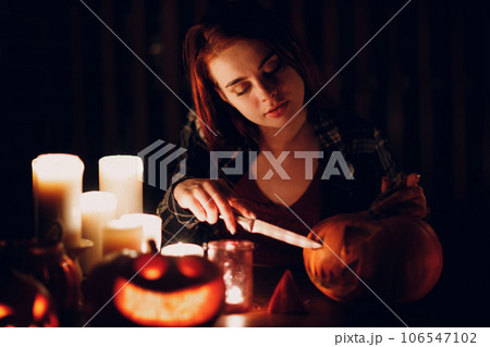 Young woman preparing Halloween pumpkin Jack-o-lantern with candles in dark. Female hands cutting pumpkins with knife 106547102