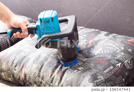 Cleaning sofa cushions with a special electric brush. Dry cleaning of upholstered furniture, close-up. Copy space for text Cleaning sofa cushions with a special electric brush. Dry cleaning of upholstered furniture, close-up. Copy space for text 106547441