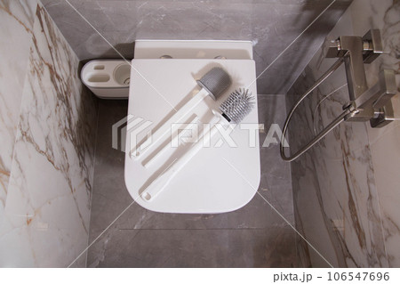 Silicone brushes for cleaning the toilet lie on the lid of the wall-hung toilet. The concept of care and cleaning the toilet from dirt and bacteria. Gray stoneware tiles on the walls, limescale Silicone brushes for cleaning the toilet lie on the lid of the wall-hung toilet. The concept of care and cleaning the toilet from dirt and bacteria. Gray stoneware tiles on the walls, limescale 106547696