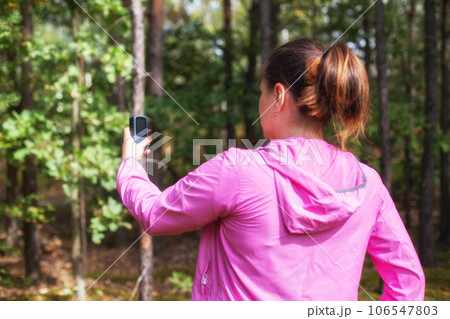 A girl in a pink sweater uses a navigator in the forest to determine her location. Mushroom picker and compass. Wandering through the forest, signal gps A girl in a pink sweater uses a navigator in the forest to determine her location. Mushroom picker and compass. Wandering through the forest, signal gps 106547803