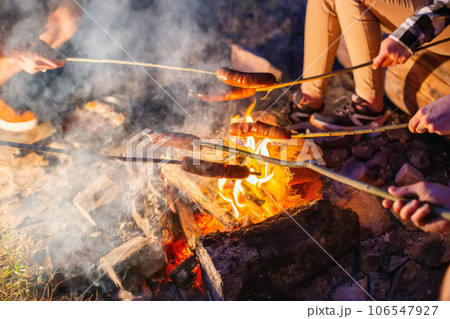 Frying sausages on a fire in nature in the evening. Outdoor cooking. Close-up Frying sausages on a fire in nature in the evening. Outdoor cooking. Close-up 106547927
