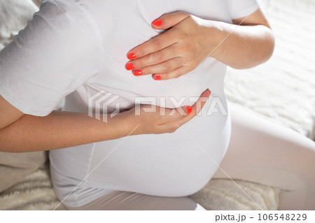 Pregnant girl holds on to the mammary gland. The concept of swelling and increase in the size of the female breast during pregnancy. Pain, close-up 106548229