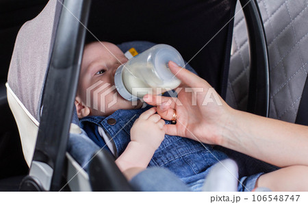 A mother feeds her baby son with milk in a car in a car seat. Safety in the car for children. Close-up A mother feeds her baby son with milk in a car in a car seat. Safety in the car for children. Close-up 106548747