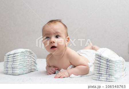 A little boy at the age of 5 months lies in a diaper on a white background and looks at the camera. Stack of diapers, anti-leak, soft and comfortable. Copy space for text 106548763