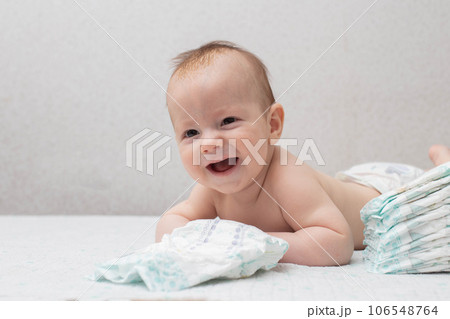 A little boy at the age of 5 months lies in a diaper on a white background and looks at the camera. Stack of diapers, anti-leak, soft and comfortable. Copy space for text 106548764
