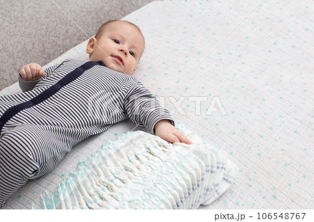 A small toddler caucasian boy in a striped suit lies on a table with a stack of diapers. Copy space for text A small toddler caucasian boy in a striped suit lies on a table with a stack of diapers. Copy space for text 106548767