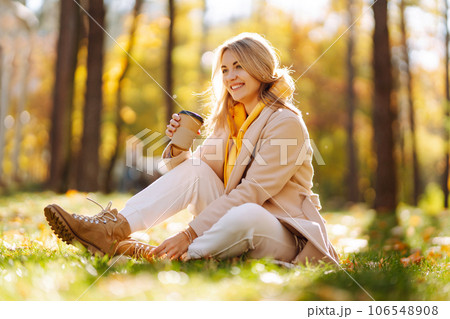 Beautiful Woman drinking coffee in autumn park. Relaxation, enjoying, solitude with nature. 106548908