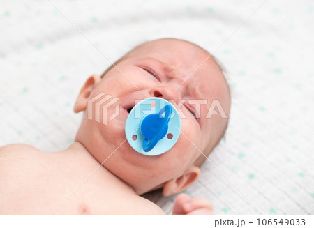 Little baby boy crying with a pacifier in his mouth. The concept of weaning the habit of sucking a pacifier in children, close-up. Copy space for text Little baby boy crying with a pacifier in his mouth. The concept of weaning the habit of sucking a pacifier in children, close-up. Copy space for text 106549033