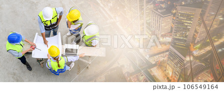 Top view of contractors, engineers and formats team in safety vests with helmets working with laptops with cityscape in night time. Banner cover design. Home building project. 106549164