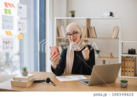 Female with yes gesture reading email via cell phone at work 106549828