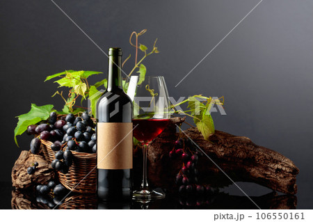 Glass and bottle of red wine with blue grapes and vine branches. 106550161