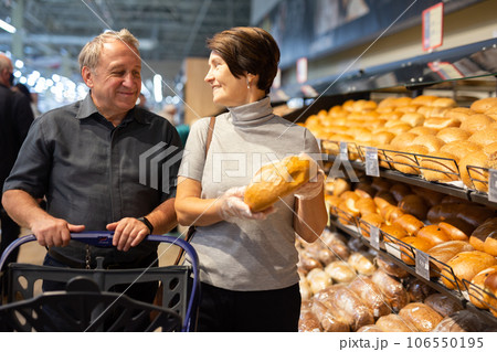 Man and woman choose hot fresh buns and bread on supermarket showcase 106550195