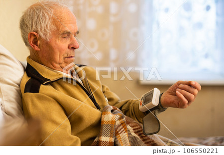 Old man wrapped in blanket measuring pressure with tonometer 106550221