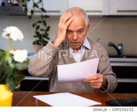 Old gray haired man sitting at table and stunned notice on white sheet 106550232