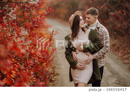 Happy and young pregnant couple in autumn park. People, lifestyle, relaxation and vacations concept. Happy and young pregnant couple in autumn park. People, lifestyle, relaxation and vacations concept. 106550457