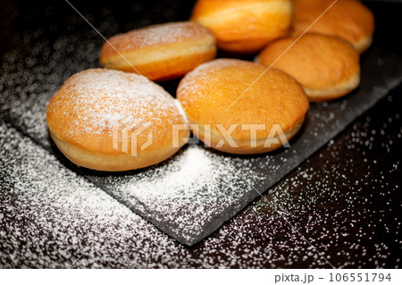 German Krapfen with drizzling glazed sprinkles in black elegant background 106551794