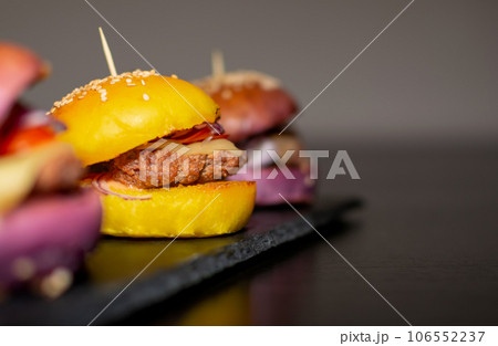 Colored Mini Gourmet Burgers with sesame seeds on black slate board Colored Mini Gourmet Burgers with sesame seeds on black slate board 106552237