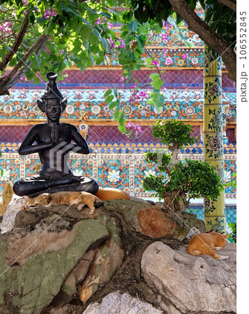 A statue of a meditating figure in a garden with orange cats and trees. A statue of a meditating figure in a garden with orange cats and trees. 106552845