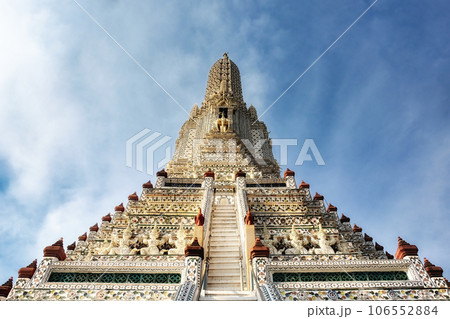 A temple in Thailand with a tall, ornate spire and a staircase leading up to it. The spire is decorated with intricate patterns and designs.The temple is made of white stone with colorful accents. A temple in Thailand with a tall, ornate spire and a staircase leading up to it. The spire is decorated with intricate patterns and designs.The temple is made of white stone with colorful accents. 106552884