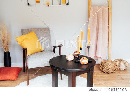 Stylish Scandinavian interior of living room with a modern armchair, coffee table with seasonal autumn decor, decorative stairs with plaid and moodboard. Cozy home interior design with a fall mood. 106553108