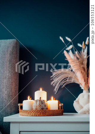 Closeup Autumn decor in stylish modern bedroom. Cozy interior with dark emerald wall, grey fabric headboard, bedside table, vase with pampas grass, pumpkin and burning candles on tray. Vertical card. 106553121