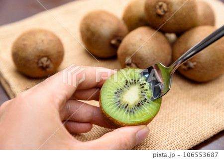 輪切りのキウイを持ちスプーンで食べる男性の手 麻袋の上に山盛りのキウイフルーツ 輪切りのキウイを持ちスプーンで食べる男性の手 麻袋の上に山盛りのキウイフルーツ 106553687