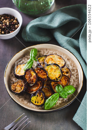 Pieces of fried eggplant with spices and basil on a plate on the table vertical view Pieces of fried eggplant with spices and basil on a plate on the table vertical view 106554622