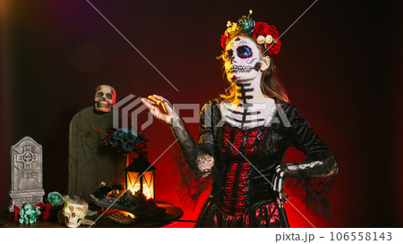 Beautiful horror woman looking at holographic image in studio, using hologram and augmented reality on dios de los muertos. Analyzing artificial intelligence and 3d, celebrating mexican tradition. 106558143
