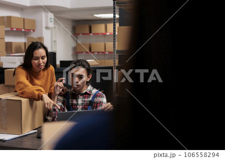 Warehouse package handlers analyzing order pick ticket on laptop while working at storage room desk. Storehouse asian workers team doing inventory management on computer together 106558294