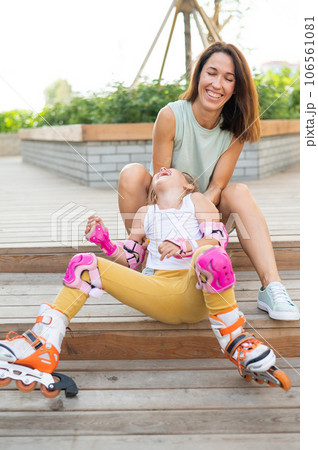 Little girl in roller skates and her mom sit on a wooden ladder and hug outdoors.  106561081