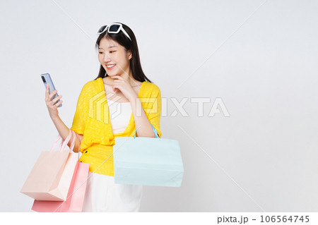 Young woman holding shopping bags while using mobile phone isolated over white background. Young woman holding shopping bags while using mobile phone isolated over white background. 106564745