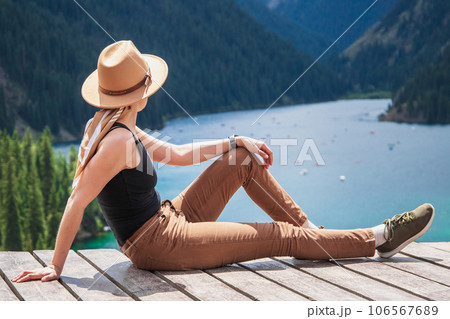 Young woman in hat is delighted, Kolsay mountain lake in Kolsai Koldery gorge near Almaty, nature of Kazakhstan National Park, Central Asia 106567689