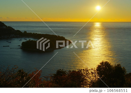 夕日で黄金色に輝く海原と港と緩やかにカーブした岬の風景 Ver3 106568551