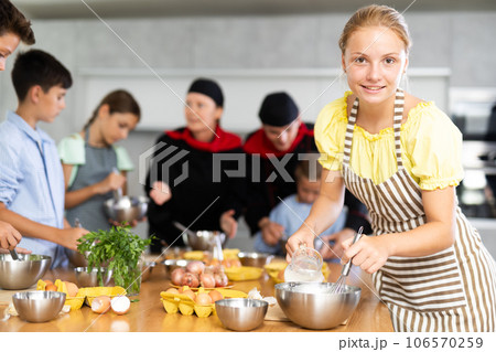 During cooking classes, girl carefully mixes ingredients in bowl with whisk. 106570259