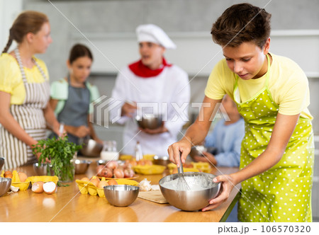 During cooking classes, teen boy carefully mixes ingredients in bowl with whisk During cooking classes, teen boy carefully mixes ingredients in bowl with whisk 106570320