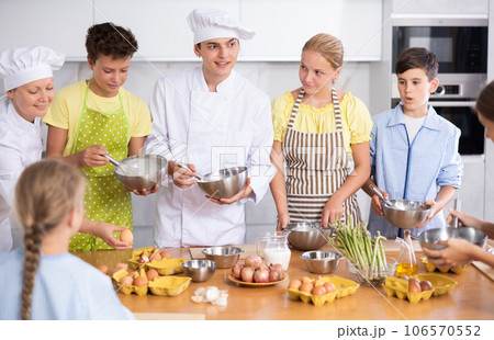 During cooking lesson, male cook tells children about culinary rules, woman assistant helps child During cooking lesson, male cook tells children about culinary rules, woman assistant helps child 106570552