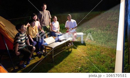 キャンプにてプロジェクターでアウトドアシアターを楽しむ人たち 106570581