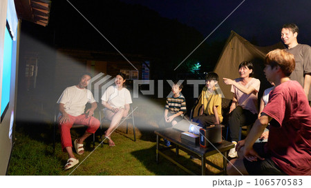 プロジェクターを使ってアウトドアで映画鑑賞をする人々 　キャンプ　ファミリー　イメージ 106570583
