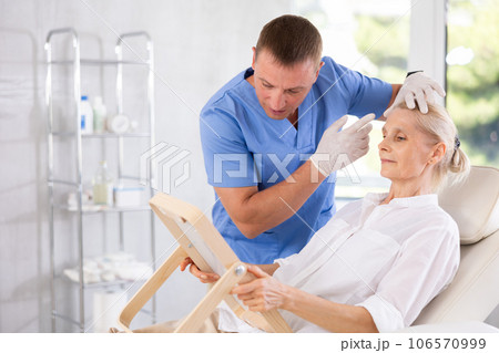 Senior woman looking at mirror while cosmetologist explaining facial procedure Senior woman looking at mirror while cosmetologist explaining facial procedure 106570999