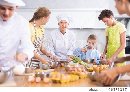 Professional female chef in white uniform conducting culinary class for tweens Professional female chef in white uniform conducting culinary class for tweens 106571017
