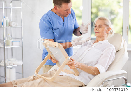 Male cosmetologist showing results of facial procedure to elderly woman Male cosmetologist showing results of facial procedure to elderly woman 106571019