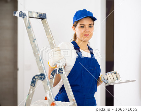 Smiling female plasterer with finishing trowel in hands at construction site 106571055