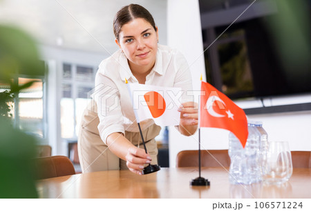 Positive young woman putting flag of Japan on the table with flag of Turkey in conference room 106571224