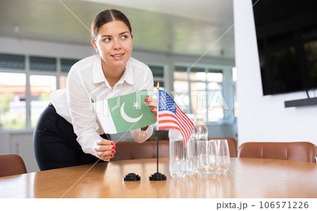 Young woman putting flags of Pakistan and USA on table in office 106571226