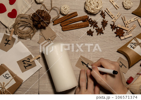 Unrecognizable young woman paint numbers on candles. Female making homemade advent calendar Made with your own hands step by step DIY crafts do it yourself. Preparation to christmas concept. Seasonal 106571374