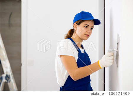Woman builder using floated trowel to daub plaster to wall 106571409
