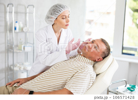 Professional cosmetologist in gloves performs a procedure on cosmetology operation of man face in clinic Professional cosmetologist in gloves performs a procedure on cosmetology operation of man face in clinic 106571428