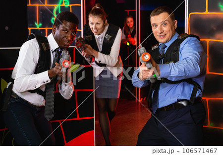Men and women in business suits playing laser tag emotionally in dark room 106571467