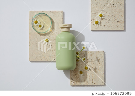 Empty label bottle displayed with stone podium. Fresh flowers featured. Chamomilla (Matricaria chamomilla) extract is a useful additive to moisturizing creams and lotions 106572099